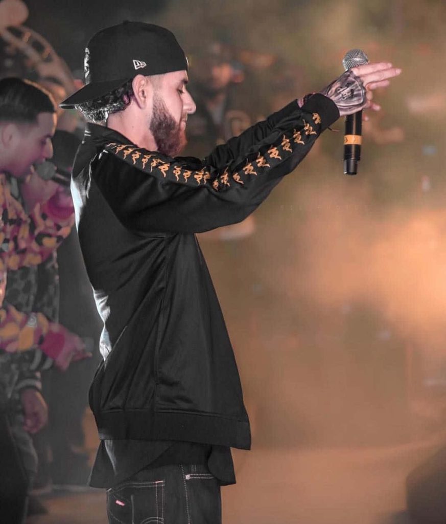 Herencia de Patrones lead singer mid-performance in black gold jacket warm concert lighting wallpaper