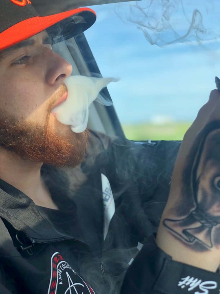 Omar Ruelas in car exhaling smoke wearing Nava Collective jacket red beard black cap wallpaper