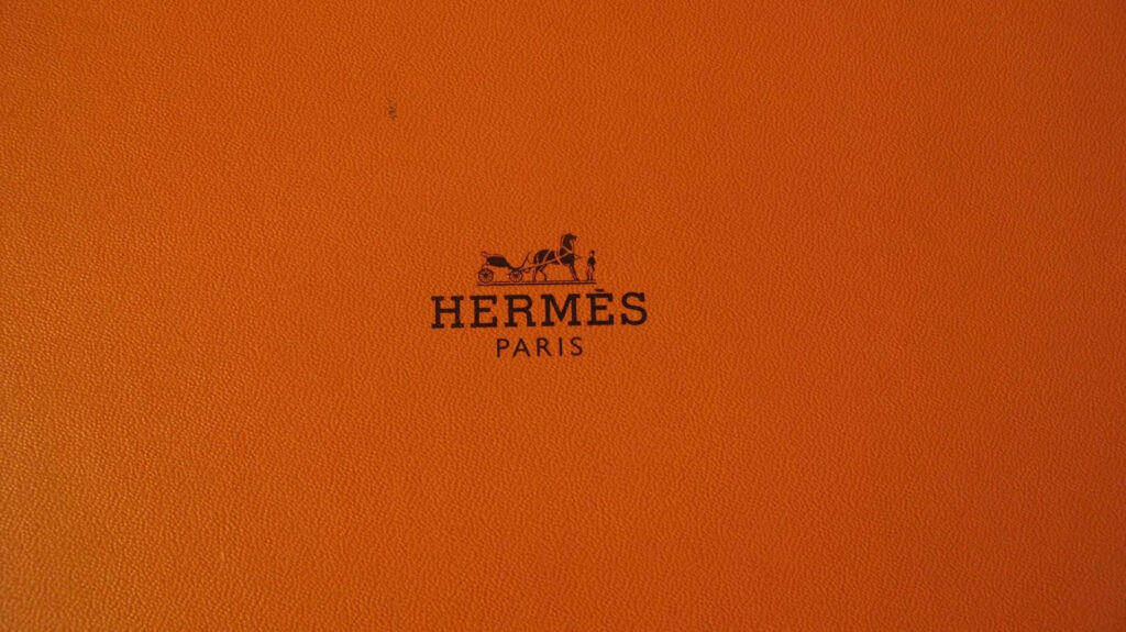 Light brown textured wallpaper with iconic Hermès Paris logo centered for luxury branding