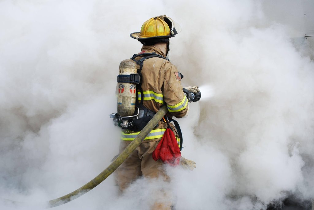 Heroic firefighter in full gear battling thick smoke holding hose emergency rescue wallpaper