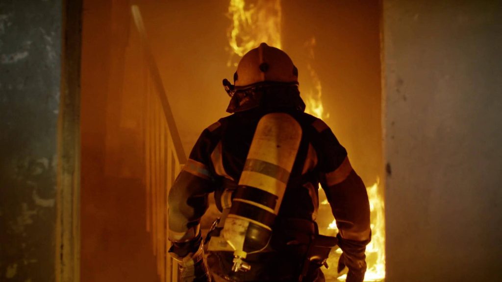 Firefighter in protective gear climbing stairs toward blazing fire rescue mission wallpaper