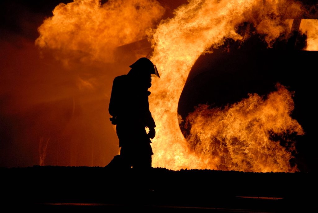 Silhouette of firefighter standing before massive blazing flames dramatic heroic emergency wallpaper