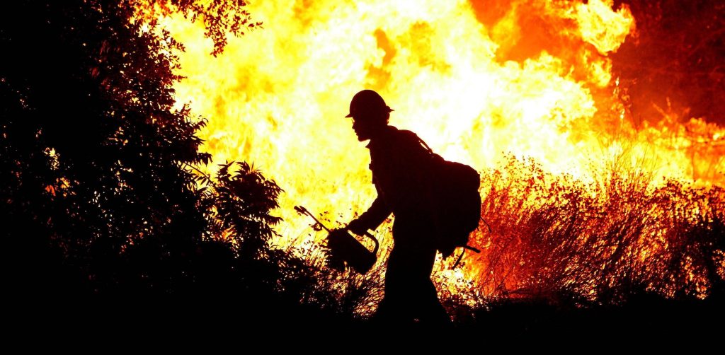 Silhouette of a firefighter battling intense forest wildfire with bright orange flames background Wallpaper
