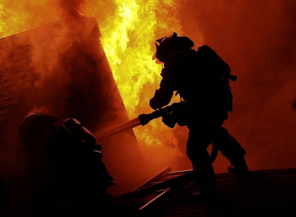 Fiery firefighter silhouette battling blaze intense orange yellow wallpaper background hero