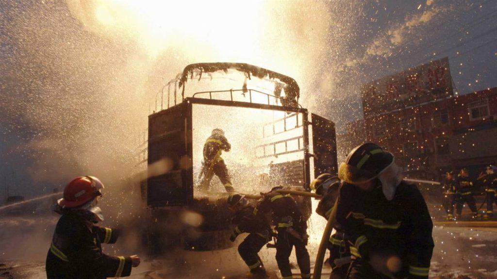 Firefighters battling explosive truck fire with sparks water spray in intense action scene Wallpaper