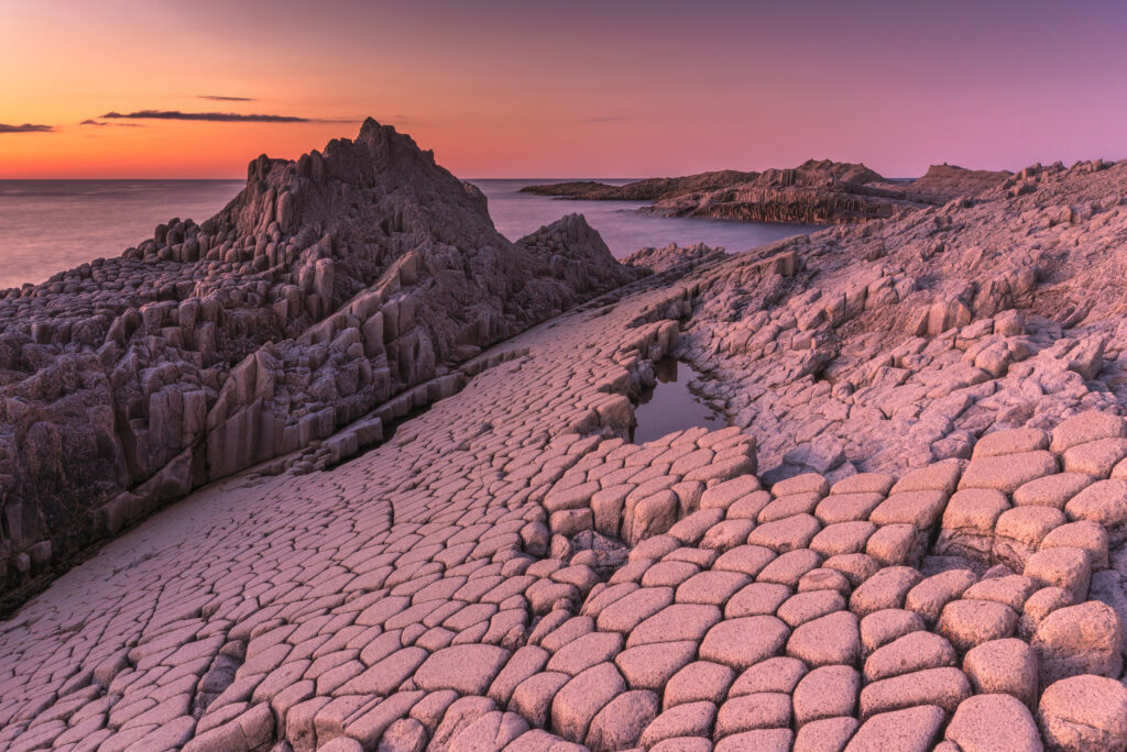 Hexagonal rocky landscape with purple orange sunset over rugged mountain peaks serene wallpaper