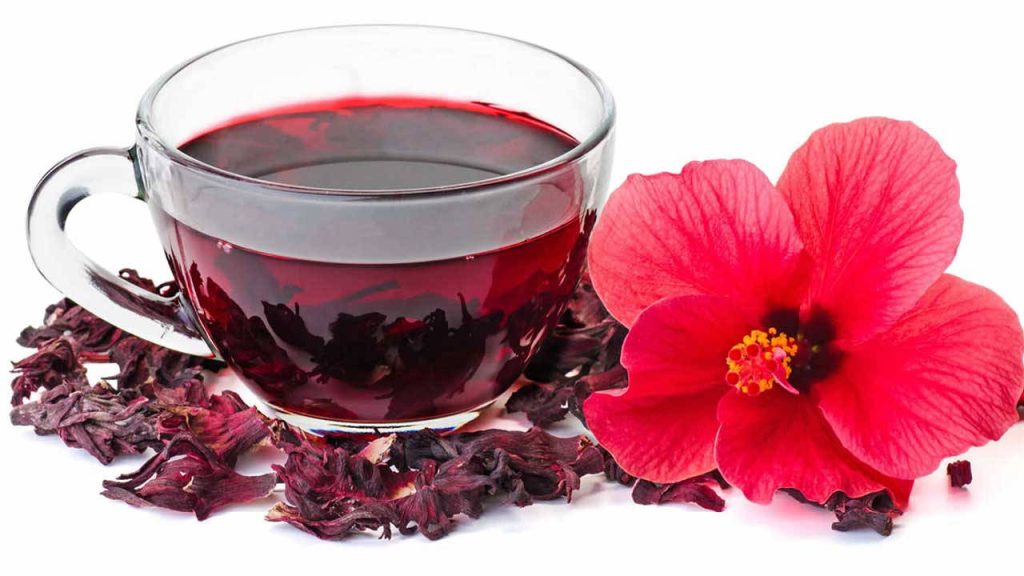 Glass cup of deep red hibiscus tea with dried calyces and fresh red hibiscus flower on white Wallpaper
