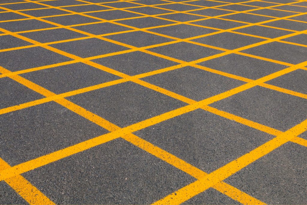 High-angle view of textured asphalt road with bright yellow geometric grid box junction pattern wallpaper