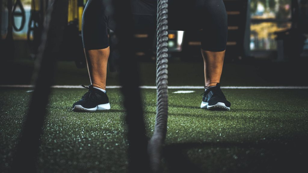 Close-up low-angle shot of athlete legs in black sneakers on turf with intense battle rope workout Wallpaper