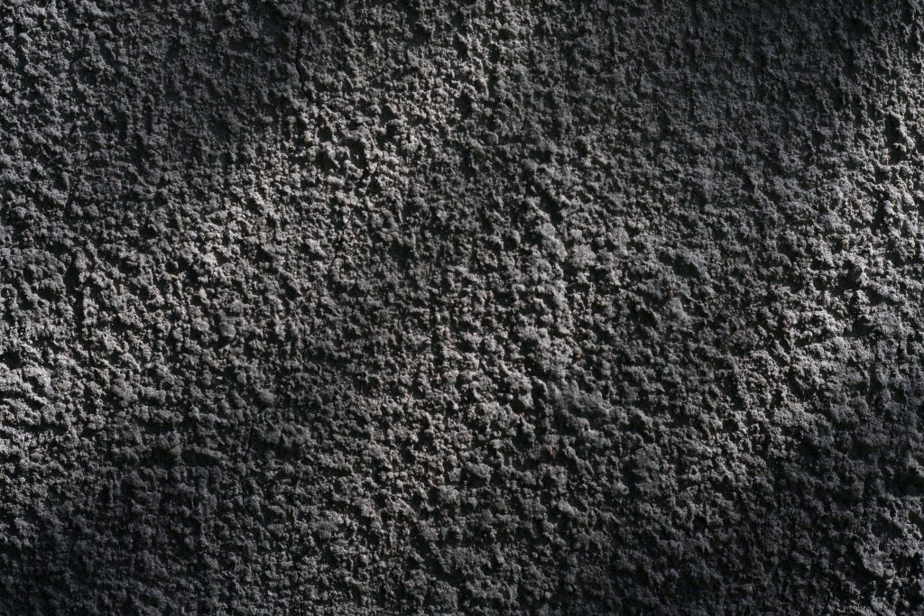 High-contrast concrete wallpaper with rough charcoal cement texture and dramatic lighting gradient