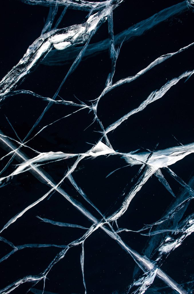 Macro shot of intricate white ice fractures glowing on dark blue frozen lake background wallpaper