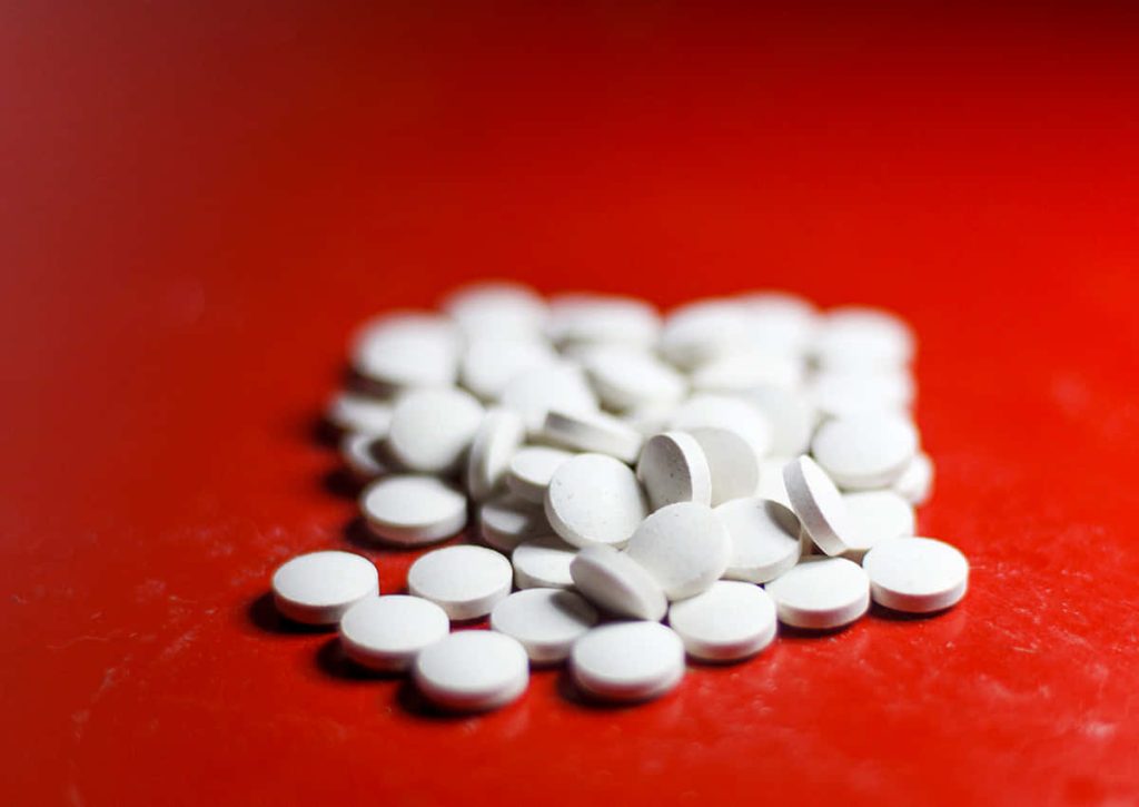 High contrast photo of small white pills scattered on vivid red background with shallow focus Wallpaper