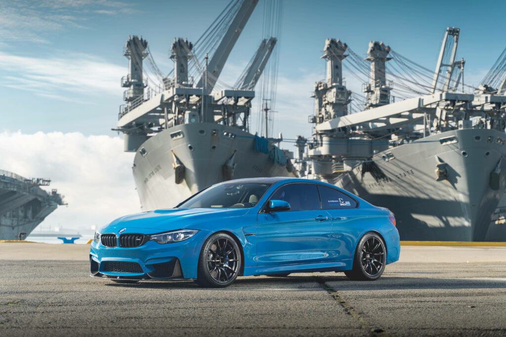 Naval Majesty: The Brilliant Blue BMW F82 M4 Shining Amidst Mighty Ships Wallpaper