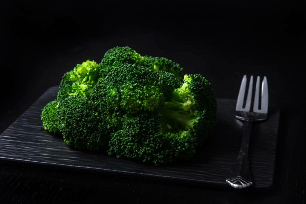 High definition dark green broccoli floret on black plate with fork dramatic lighting healthy food Wallpaper
