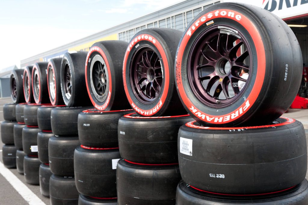 High-definition racing wallpaper with stacked Firestone Firehawk tires in professional pit lane