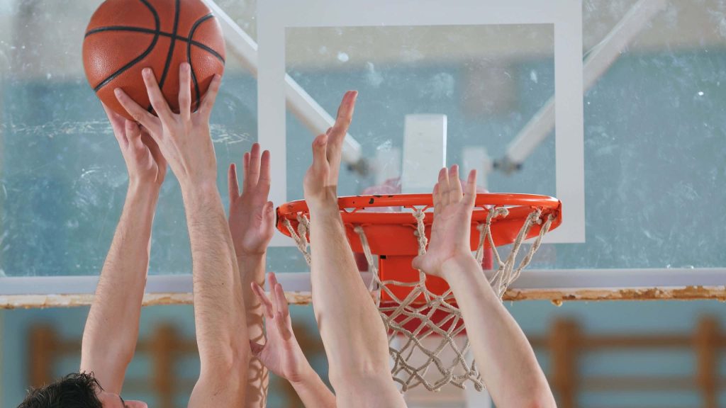 Dynamic basketball action with multiple hands reaching for ball near rim on indoor court wallpaper