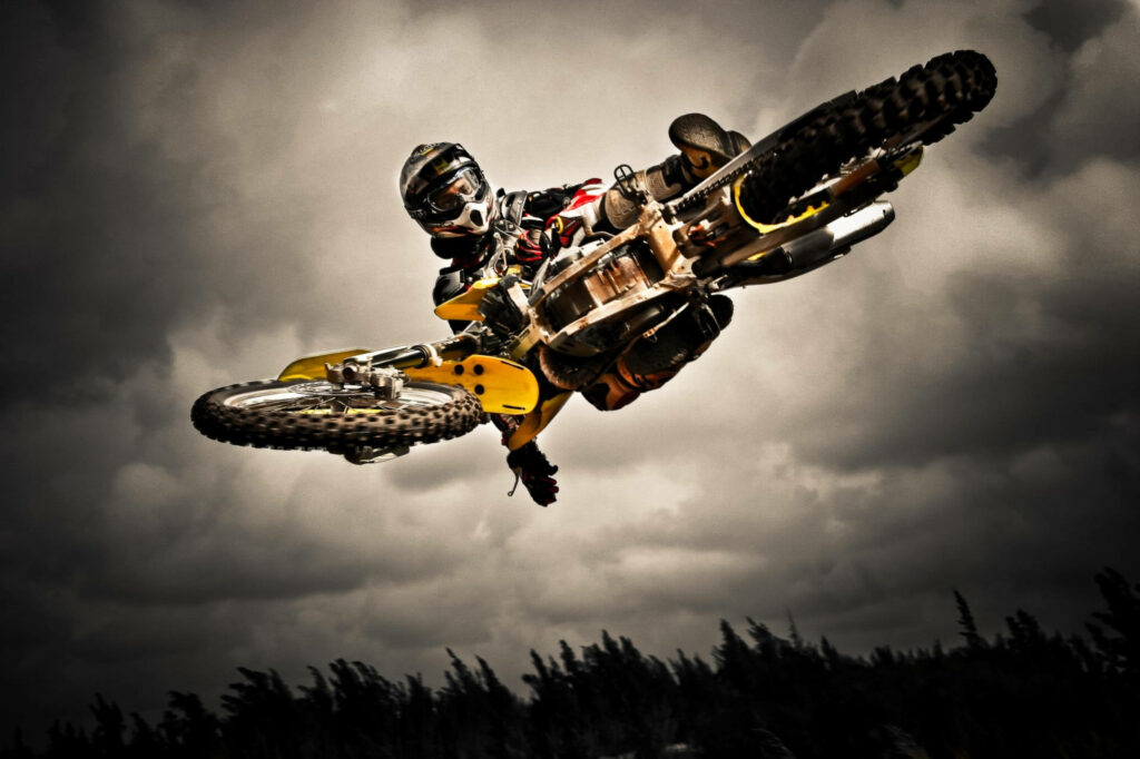 High-Flying Dirt Bike Stunt Against Dramatic Cloudy Sky Wallpaper