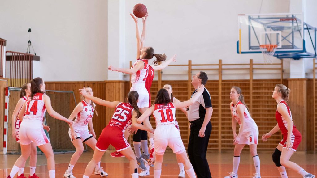 Women basketball players jump ball intense game gymnasium court red white uniforms wallpaper