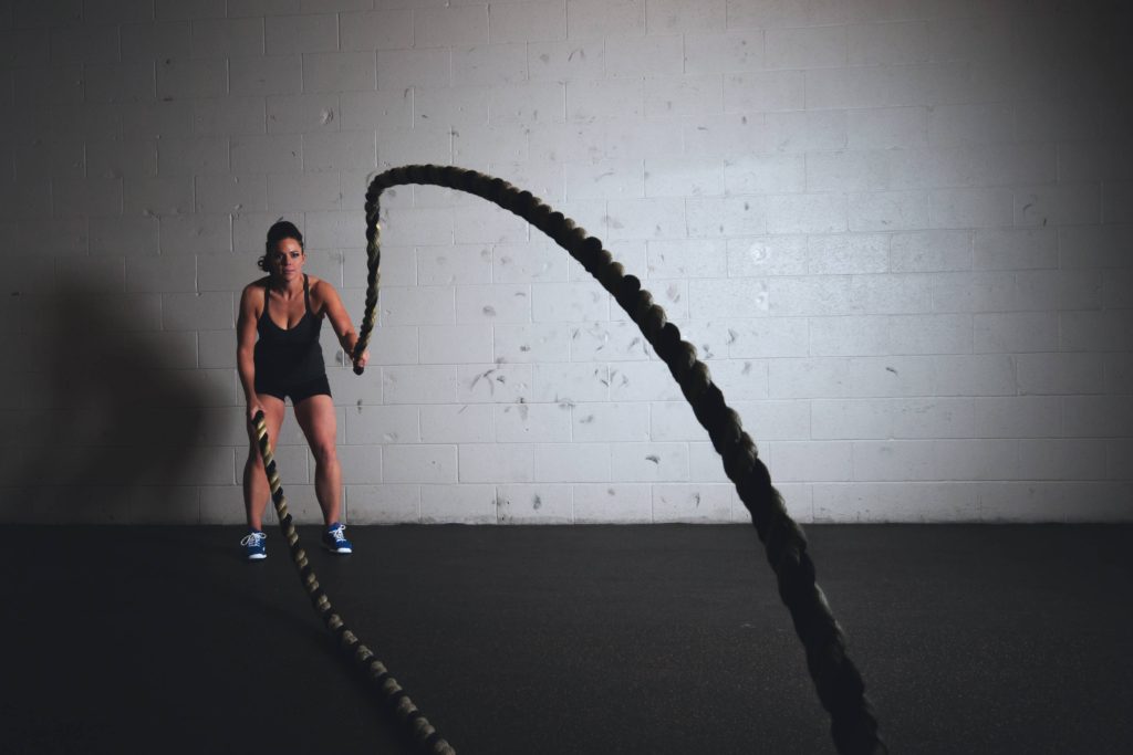 Fit woman using battle ropes gym wallpaper with white brick wall fitness motivation background