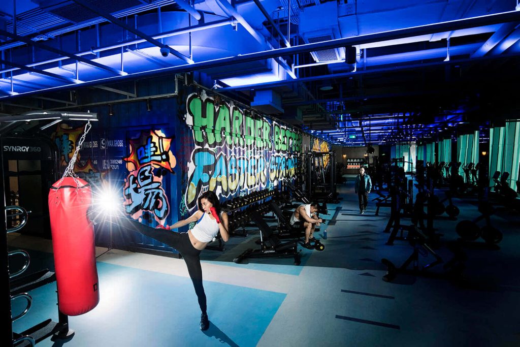 Determined woman kicks red heavy bag in blue-lit gym with graffiti decor high-intensity workout Wallpaper