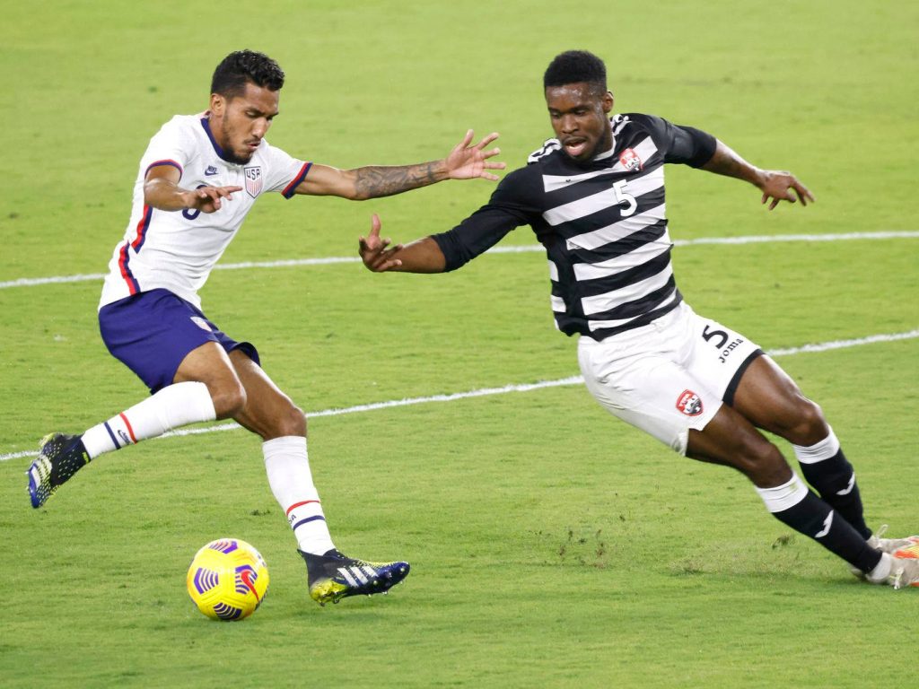USMNT player dribbling past Trinidad and Tobago defender in bright daylight soccer action Wallpaper