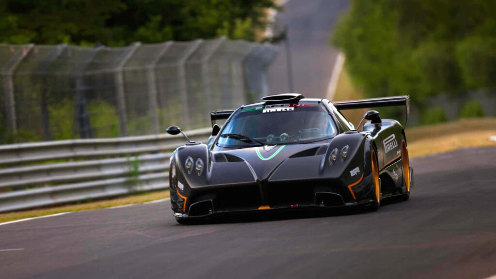Black race car speeding on winding track with greenery and safety barriers race wallpaper background