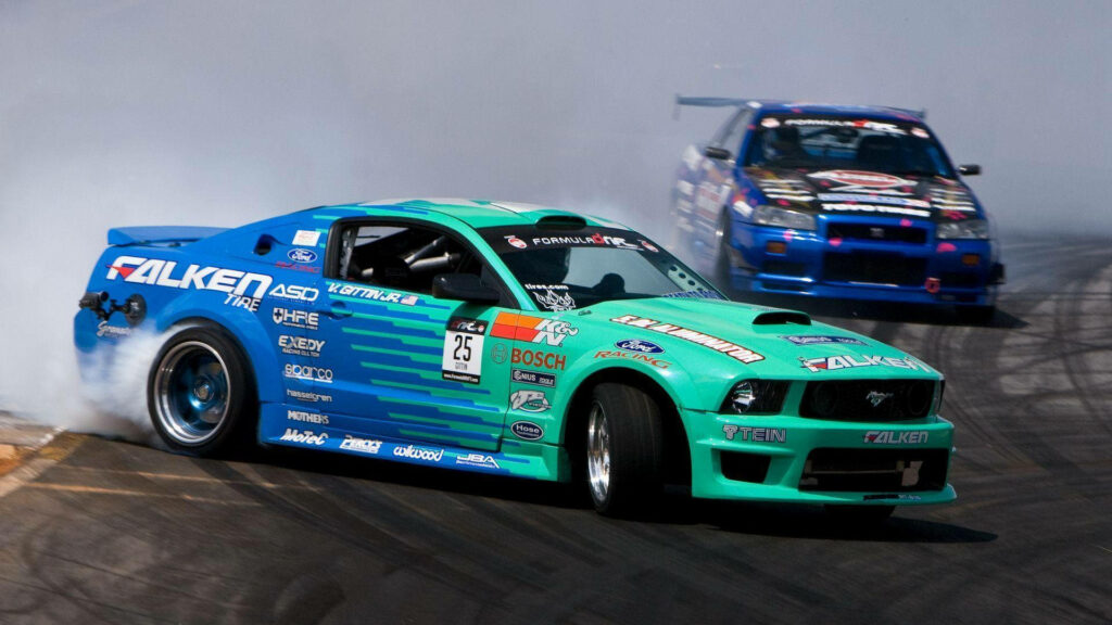 Two drift cars blue and green race side by side through smoke on a racing track wallpaper background