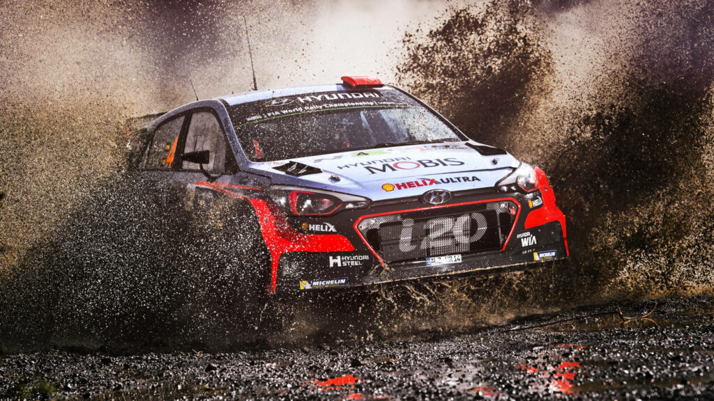 High performance rally car racing on muddy road kicking up dirt and water dynamic action wallpaper