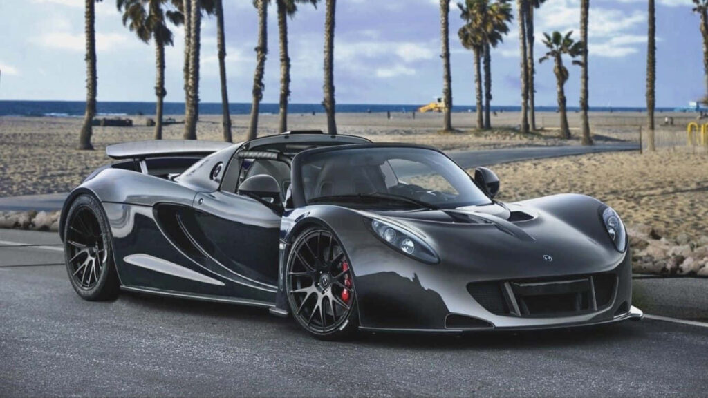 High-performance sports car parked by palm-lined beach under partly cloudy sky wallpaper background