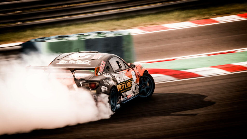 High-powered drift car speeds around racetrack corner with tire smoke motorsport action wallpaper