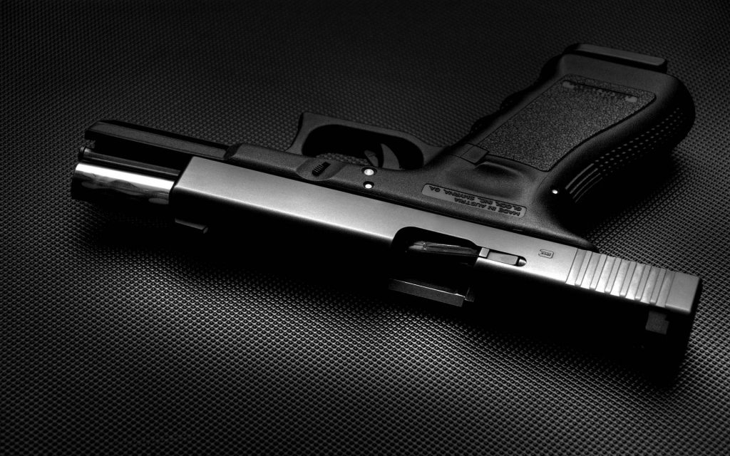 Black Glock pistol slide locked open on dark textured surface with dramatic studio lighting background Wallpaper