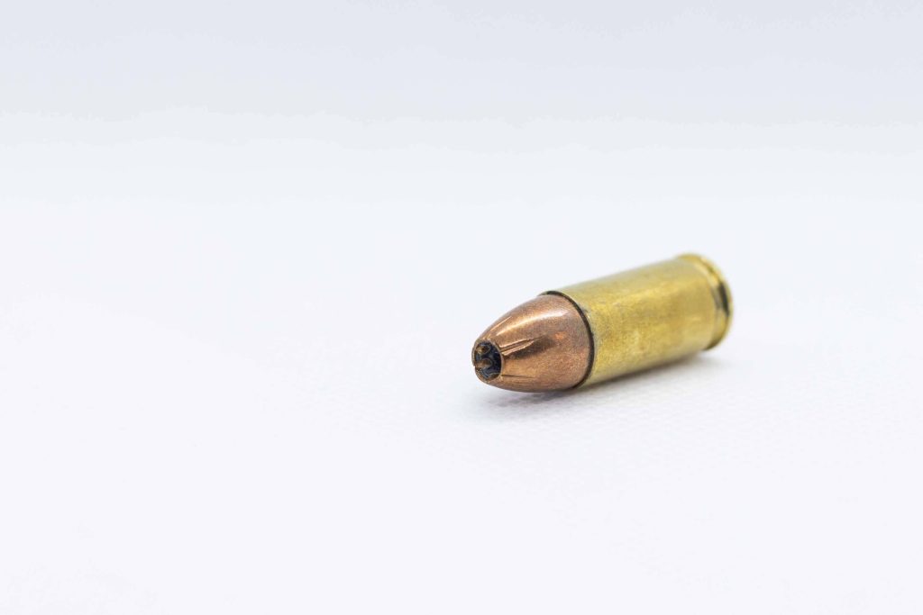 Macro close-up of a jacketed hollow point handgun cartridge with copper tip on white background Wallpaper