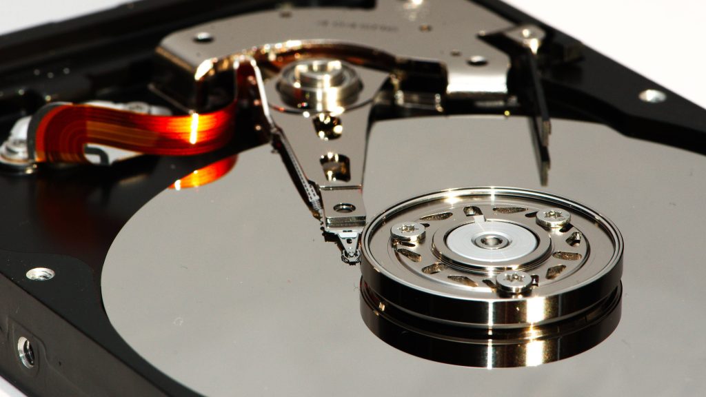 Macro close-up of an open magnetic hard drive showing reflective platter and actuator arm details Wallpaper