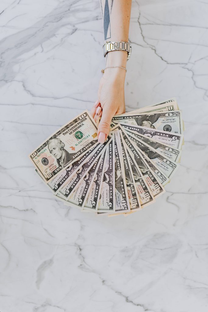 Manicured hand holding mixed US dollar bills on white marble high-resolution wallpaper background