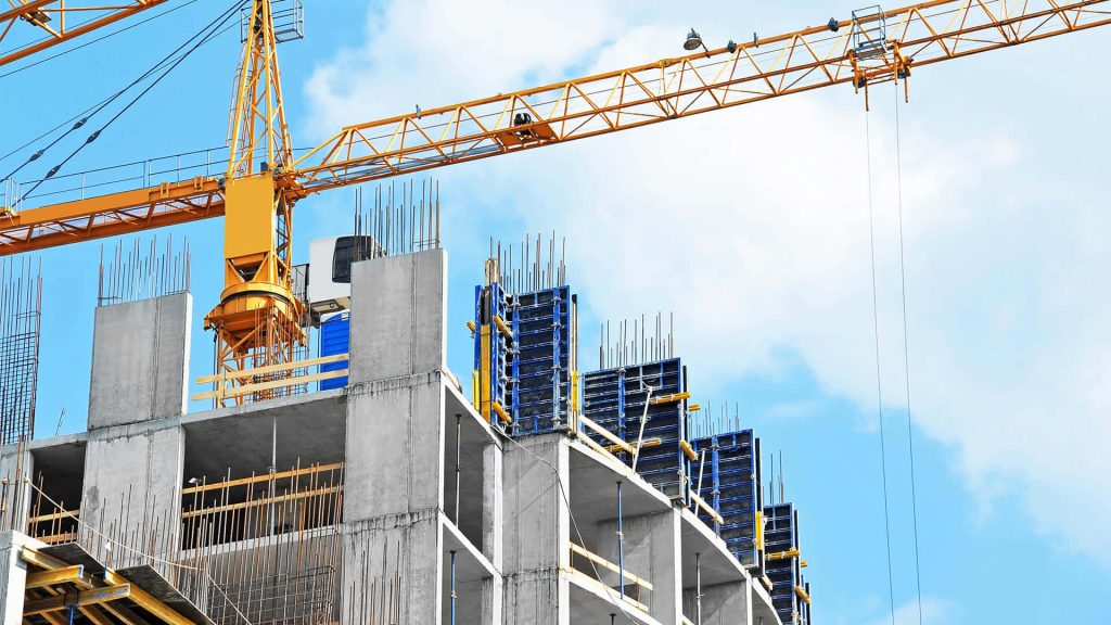 Yellow tower crane over concrete high-rise construction with steel rebar and blue formwork panels Wallpaper