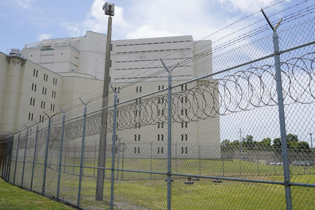 High-security prison with razor wire fence against bright daytime sky and off-white building Wallpaper