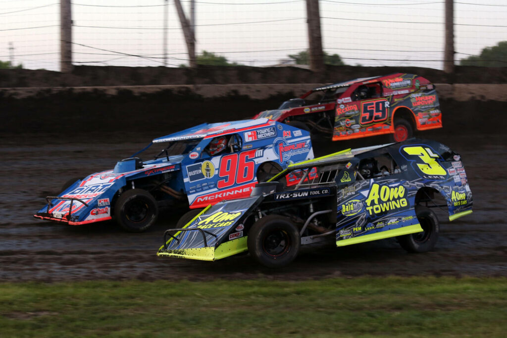 High-speed dirt track race with three colorful modified cars kicking up dust and motion blur Wallpaper