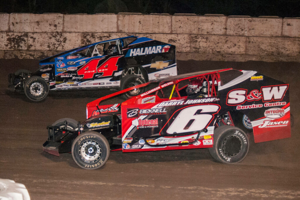 Two modified dirt track race cars in red and blue speeding on a clay oval at night wallpaper