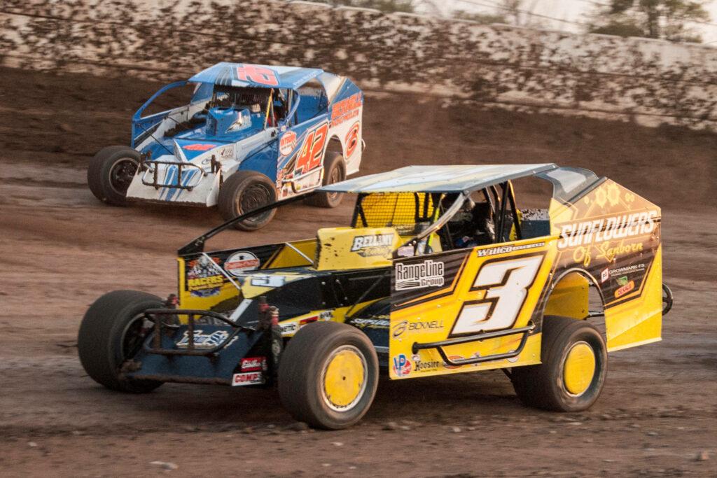 Two modified race cars speeding on rugged dirt track with flying dust in thrilling dirt racing action Wallpaper
