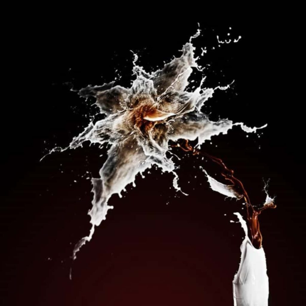 High-speed splash of white milk colliding with dark coffee on black background wallpaper