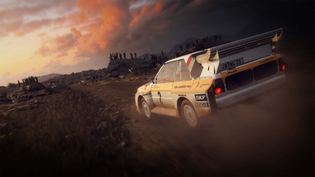 Rally car racing on dusty dirt track with dramatic clouds and spectators on rocky terrain wallpaper