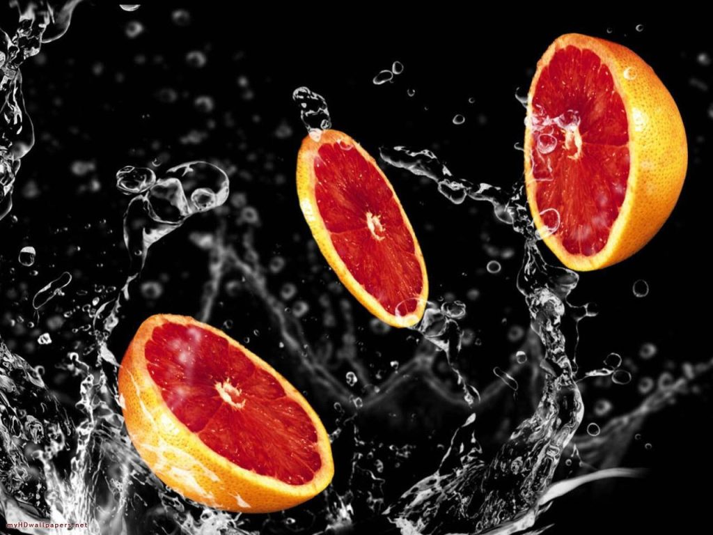 High-speed photo of three vibrant sliced red grapefruits splashing in water on black background Wallpaper