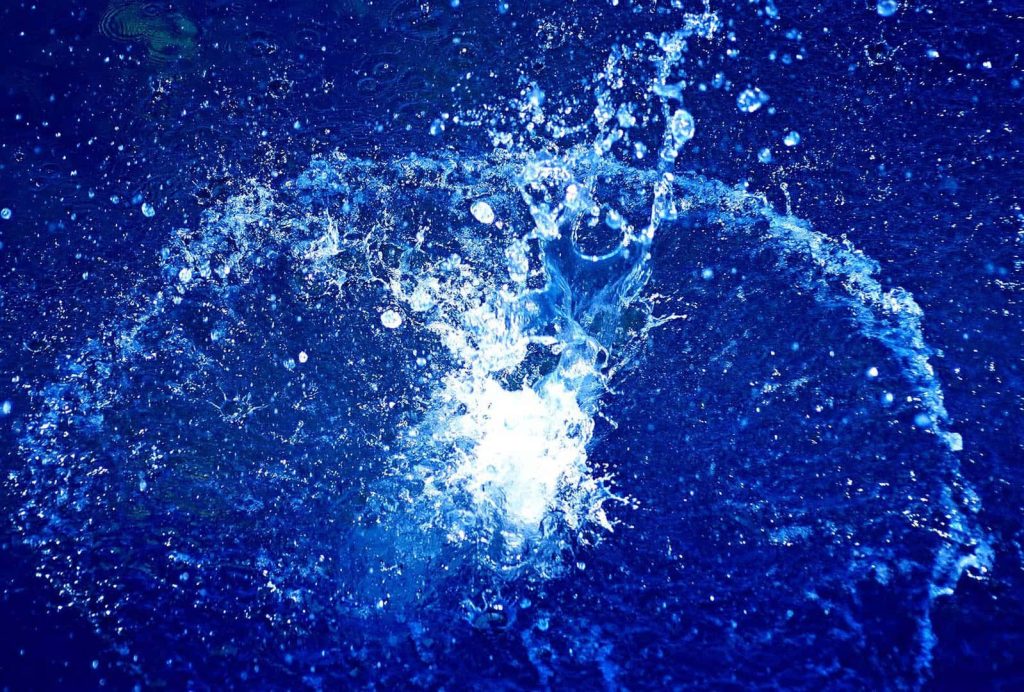 High-speed water splash with sparkling droplets on vibrant deep blue background wallpaper
