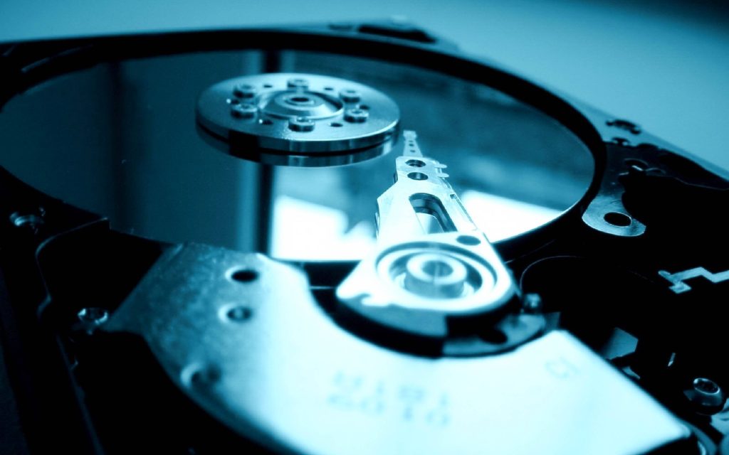 Macro shot of hard disk drive with blue light highlighting metallic platter and actuator arm Wallpaper