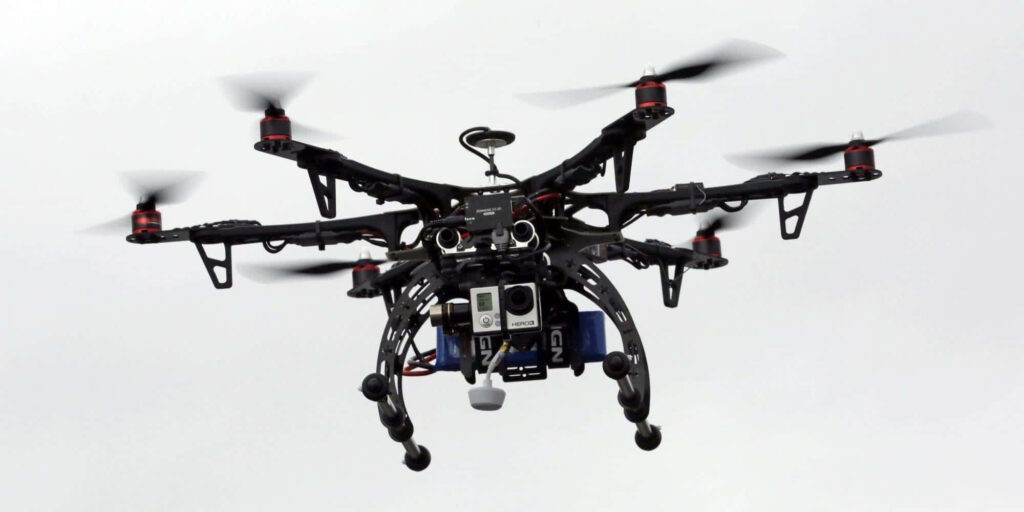 High-tech black drone with multiple propellers and camera flying against white sky background Wallpaper