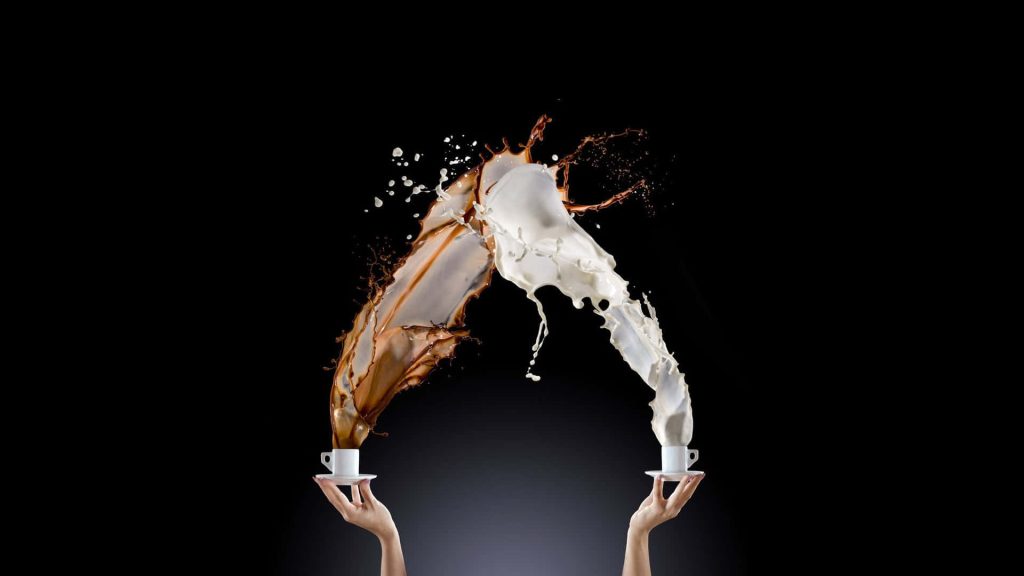 Two hands splash coffee and milk from white cups in a fluid arch on black background wallpaper