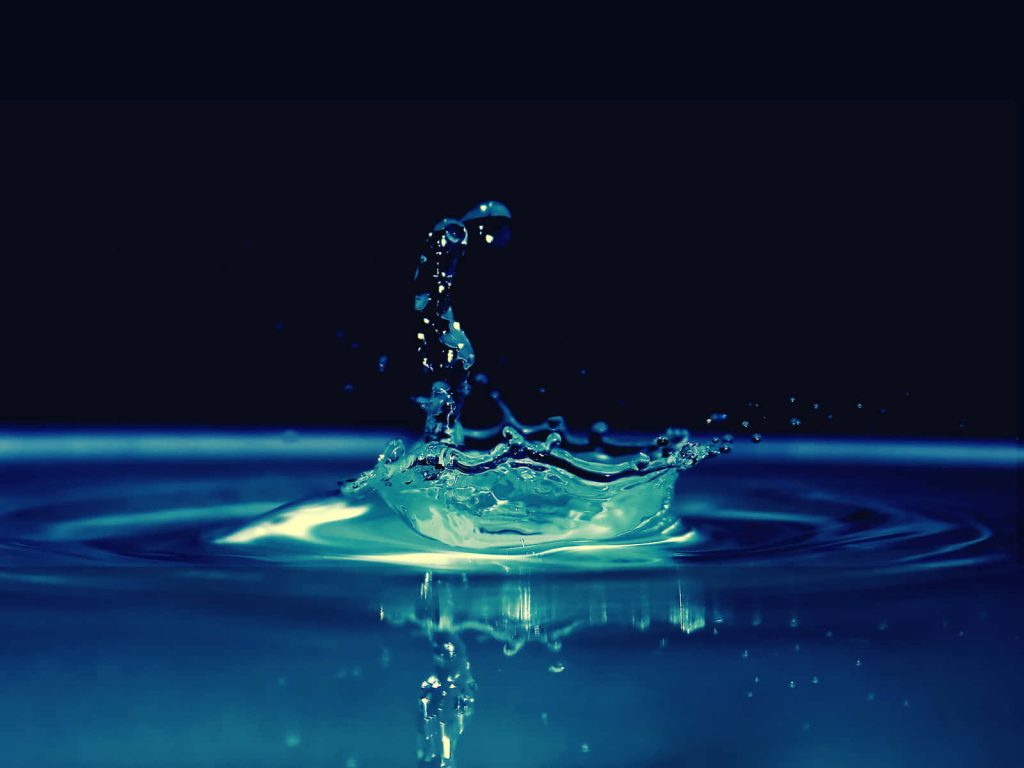 High-speed cyan water drop splash on deep blue reflective surface with black background wallpaper