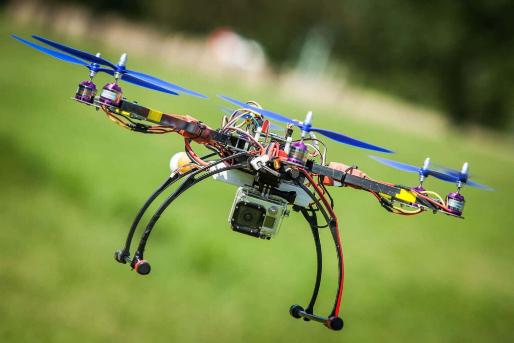 High-tech drone with blue propellers and camera flying over blurred green landscape in sunlight Wallpaper
