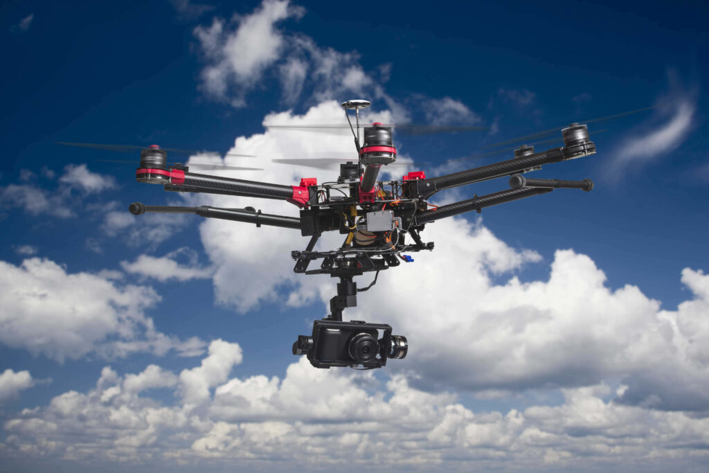 High-tech drone with mounted camera hovering against bright blue sky and white clouds background Wallpaper
