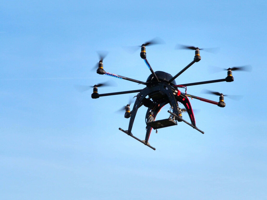 Sleek multi-rotor drone hovering in clear blue sky showcasing high-tech design and precision engineering Wallpaper